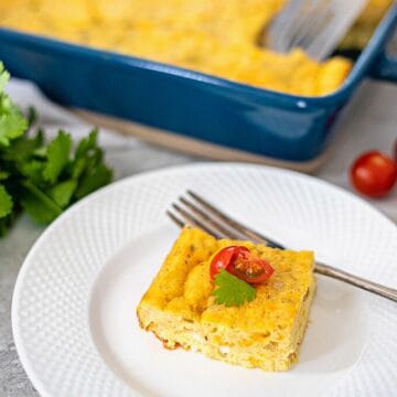 Slice of green chile egg casserole topped with fresh tomato on a white plate.
