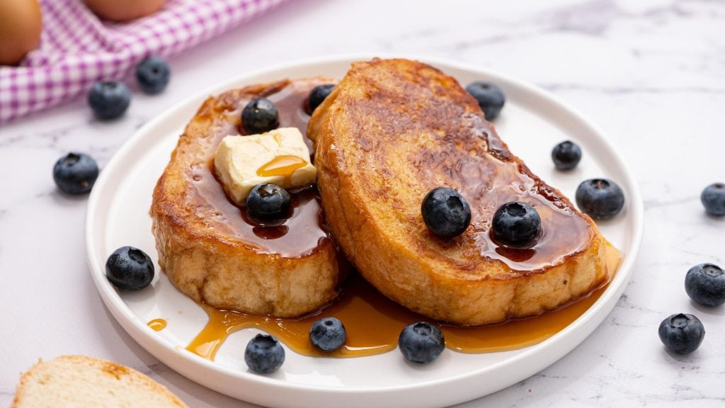 Platter of French Toast with berries and maple syrup and white plate with french toast