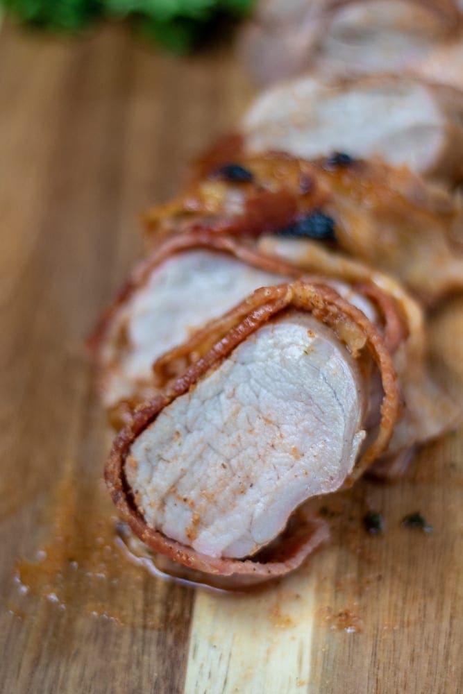 Bacon Wrapped Pork Tenderloin sliced on wooden cutting board.