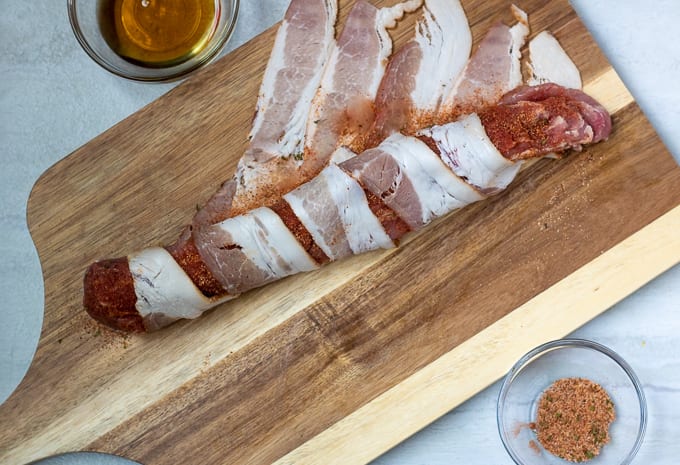 Bacon being wrapped around pork tenderloin.