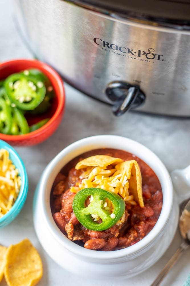 Bowl of Chili  topped with cheese next to Crockpot.