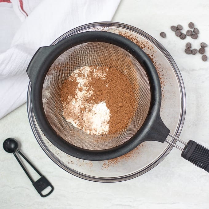 Brownie ingredients being sifted into large mixing bowl.