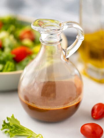 Balsamic Dressing in glass pitcher next to tossed salad.