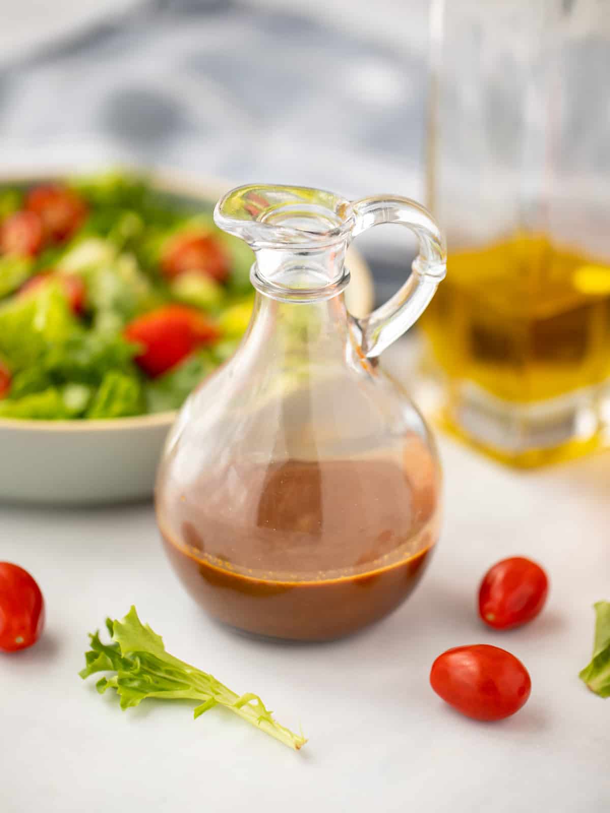Balsamic Dressing in glass pitcher next to tossed salad. 