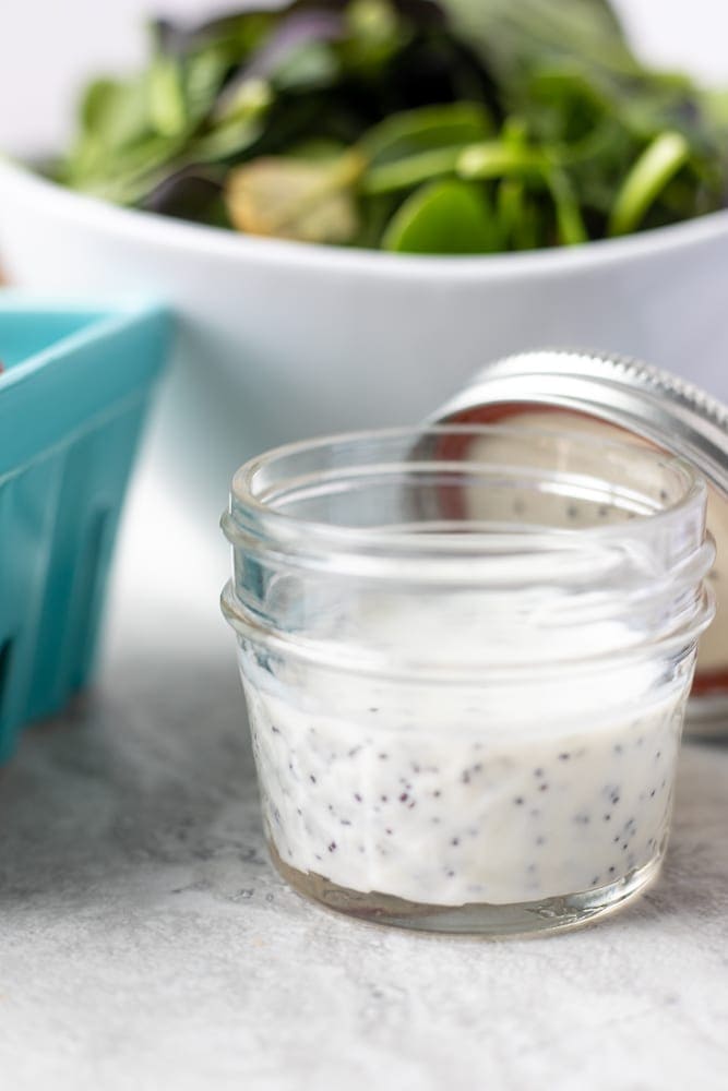 Creamy Poppy Seed Salad Dressing in small glass jar next to mixed greens.