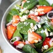 Spinach with strawberries, shallots, and feta in white bowl