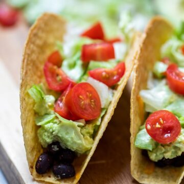 Close up of baked black bean tacos topped with lettuce and tomatoes.