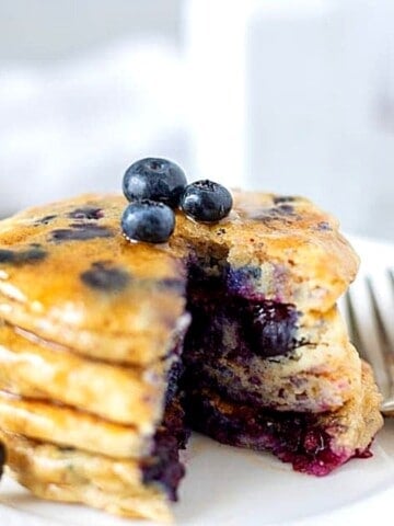 Stack of blueberry pancakes on white plate with fork.
