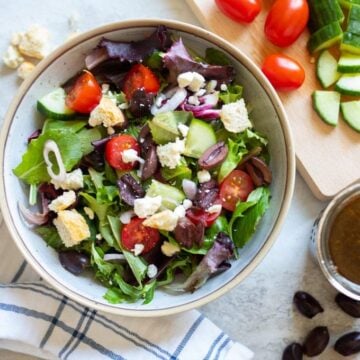 Greek Salad next to cutting board with fresh veggies
