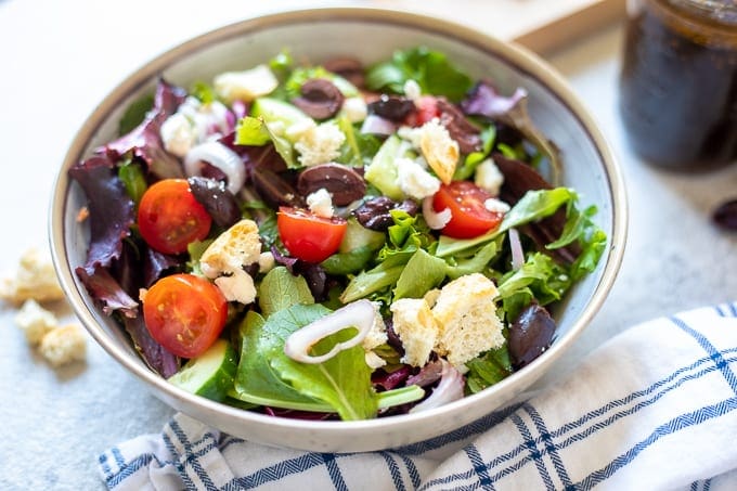 Greek Salad in a White Bowl with greek dressing to side. 