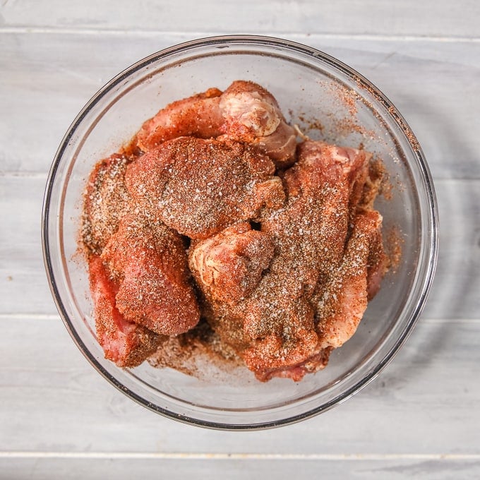 Pork Shoulder cut into chunks rubbed with homemade rub in a clear mixing bowl. 