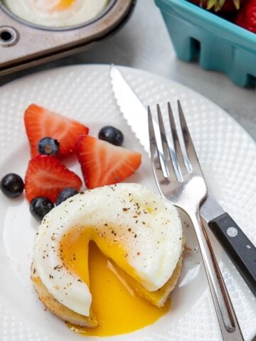 Poached egg cut open to reveal runny yolk on white plate