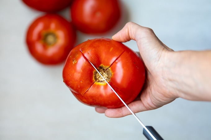 Knife scoring an x into the top of a vine ripened tomato
