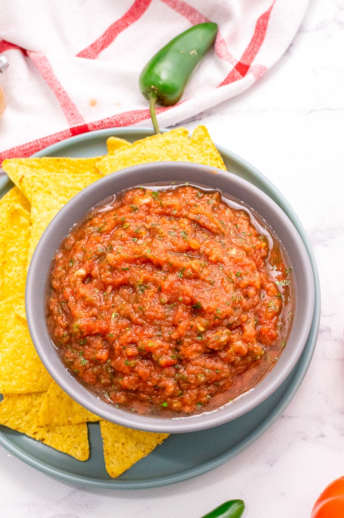 Salsa in white dish with chip dipping into the fresh salsa