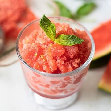 Watermelon Granita in Glass Dish topped with fresh mint and fresh watermelon in background.
