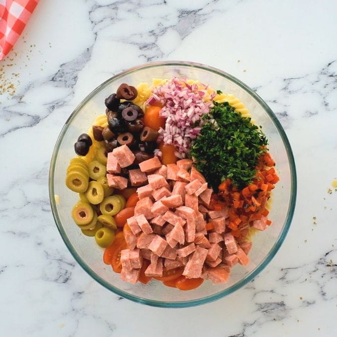 Pasta with all the toppings for antipasto pasta salad in glass bowl.