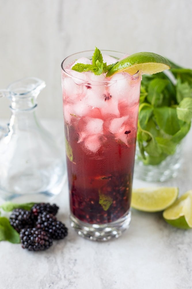 Blackberry Mojito in clear glass with limes and mint.