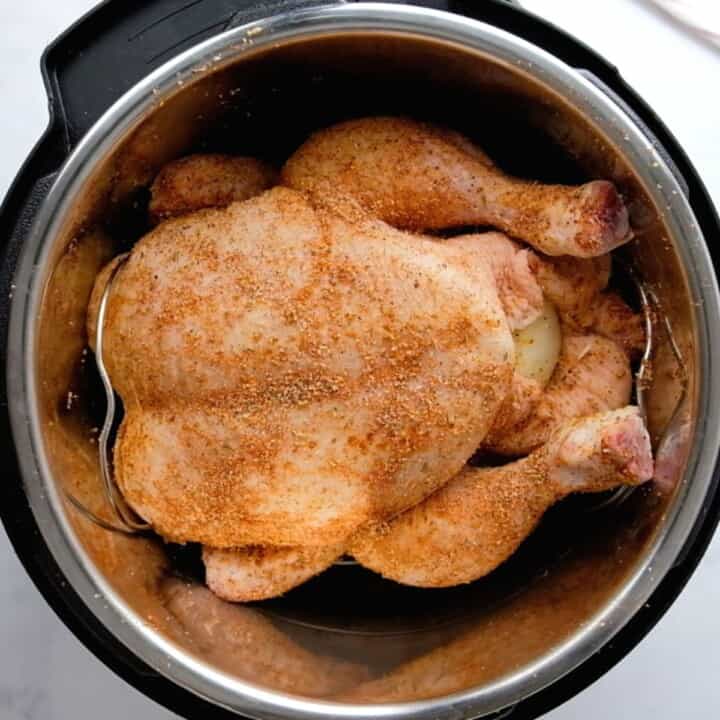 Whole seasoned chicken on trivet inside inner pot.