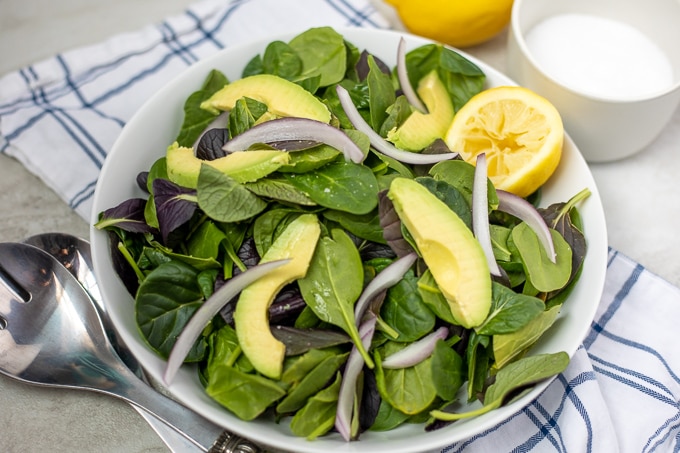 Bowl with spinach, avocados, and red onions and lemon.