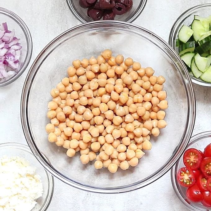 Ingredients for Chickpea Salad in clear bowls on white counter