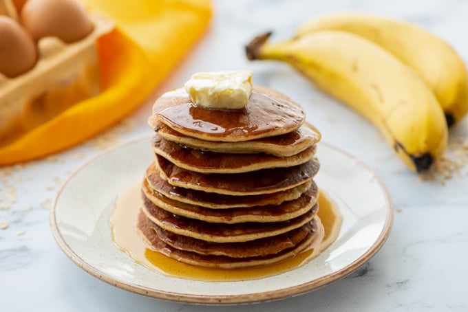 Stack of Blender Oat Pancakes on plate with bananas in back.
