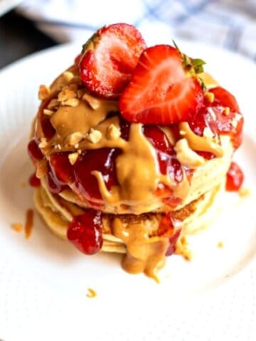 Stack of peanut butter pancakes topped with strawberry sauce and peanut butter syrup.