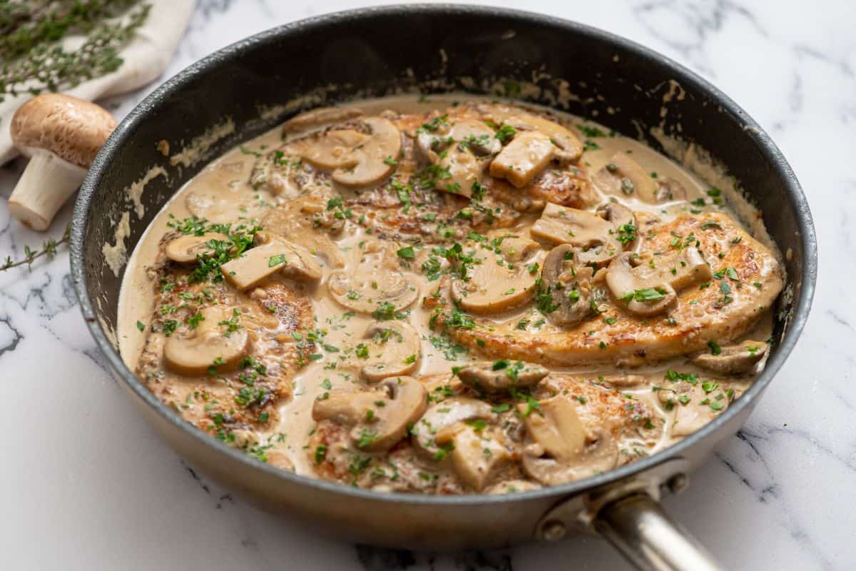 Skillet with prepared chicken marsala and topped with parsley.
