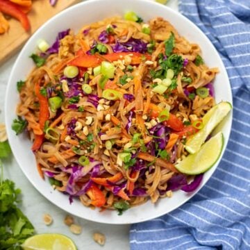 White Bowl filled with peanut noodles topped with fresh vegetables and limes on the side