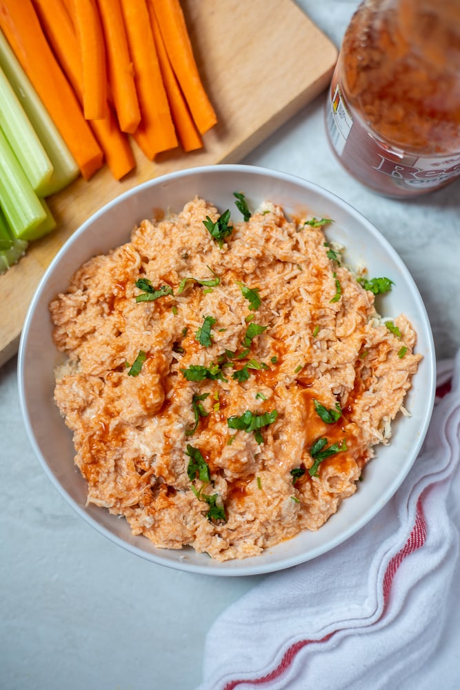 Shredded Instant Pot Buffalo Chicken in white dish next to carrots and celery