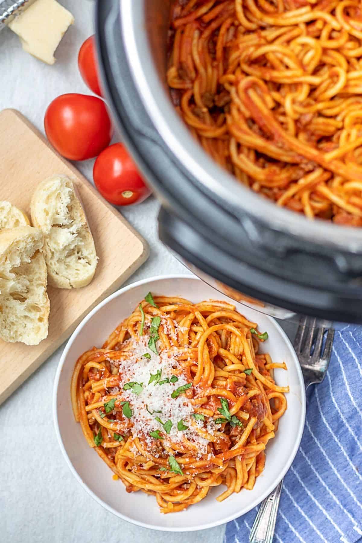 Spaghetti in white bowl next to Instant Pot in inner pot. 