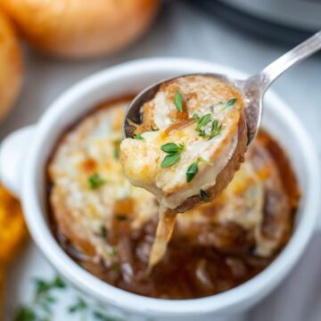 Bowl of French Onion Soup with spoon pulling out cheesy topper