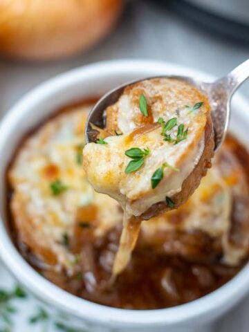 Bowl of French Onion Soup with spoon pulling out cheesy topper
