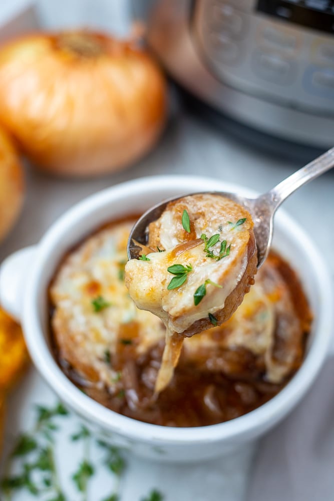 Bowl of Instant Pot French Onion Soup with spoon pulling out cheese pull.