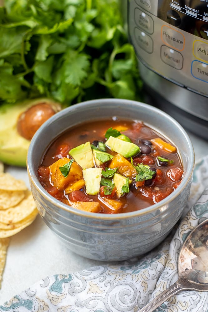 Bowl of Sweet Potato Chili next to Instant Pot topped with diced avocado.