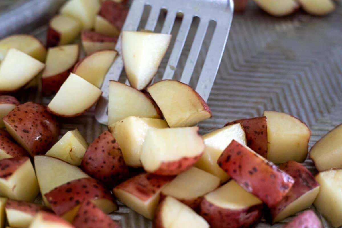 Spatula flipping red potatoes on sheet pan. 