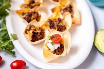 Taco Cups on white platter topped with tomatoes and sour cream.