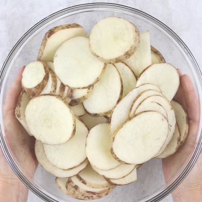 Thinly sliced potatoes in mixing bowl.