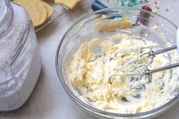 Mixing Bowl with Butter and Cream Cheese Creamed in it next to baked sugar cookies.