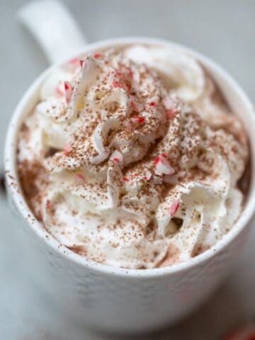 Close up of mug of hot chocolate topped with whipped cream and crushed peppermints.