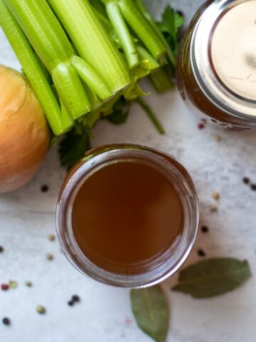 Jar of homemade vegetable broth next to onions and celery