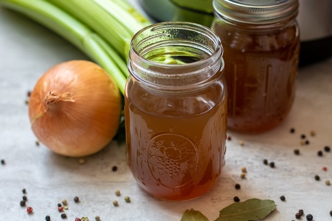 Vegetable Broth in Clear Glass jar next to onion and celery