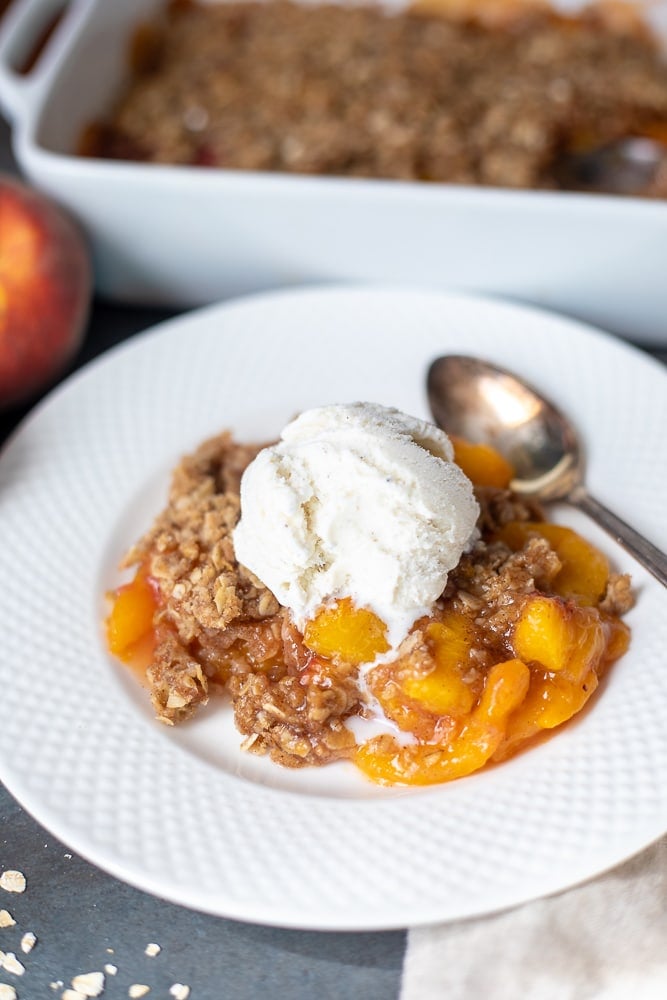 Peach Crisp on white plate topped with ice cream