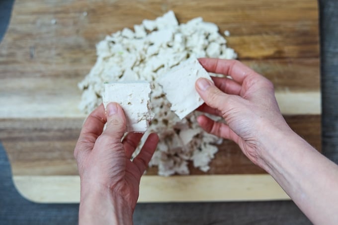 Tearing tofu into small pieces over cutting board.