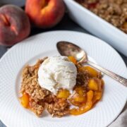 Peach Crisp dished out in white bowl with vanilla ice cream