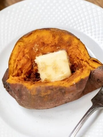 Baked Instant Pot Sweet Potato on white plate topped with pat of butter.