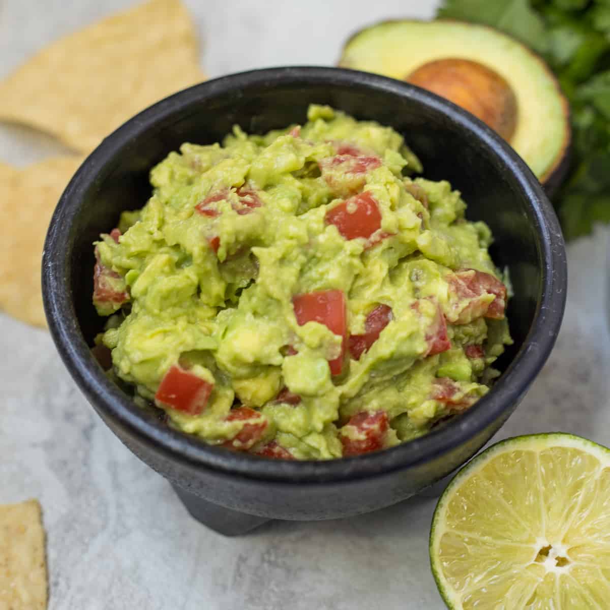 Guacamole in white bowl next to chips.