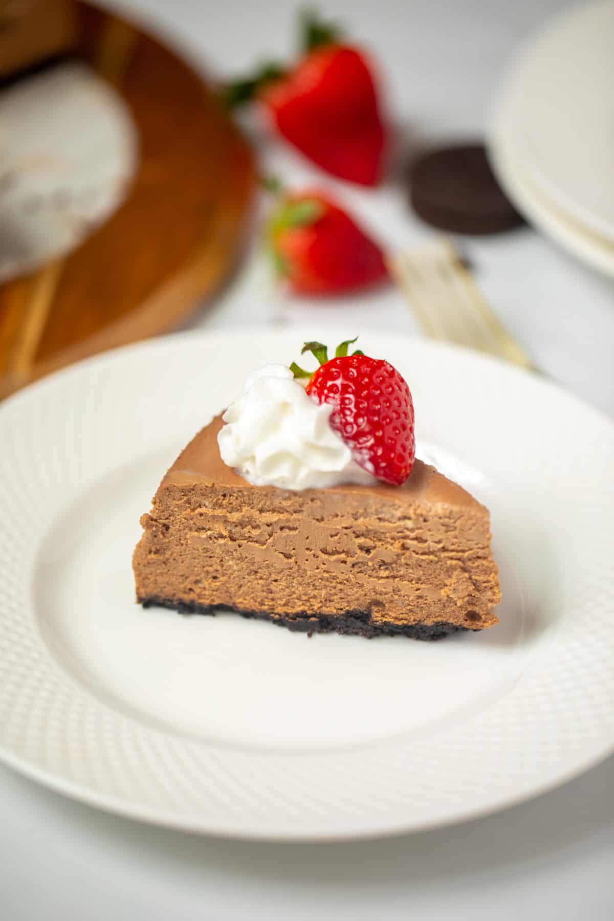 Slice of chocolate cheesecake on white plate topped with whipped cream and strawberry.