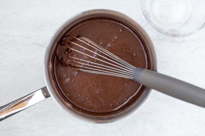 Saucepan with chocolate syrup and whisk.