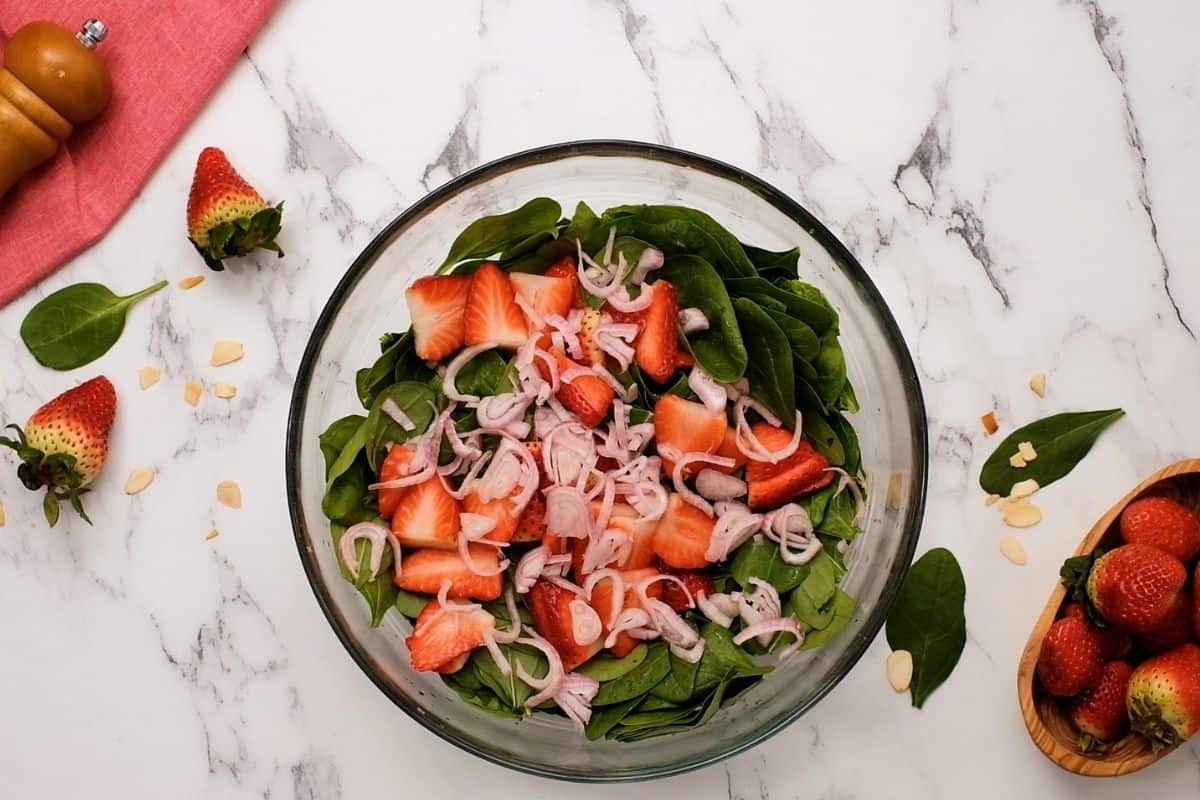 Strawberries and shallots on top of spinach. 