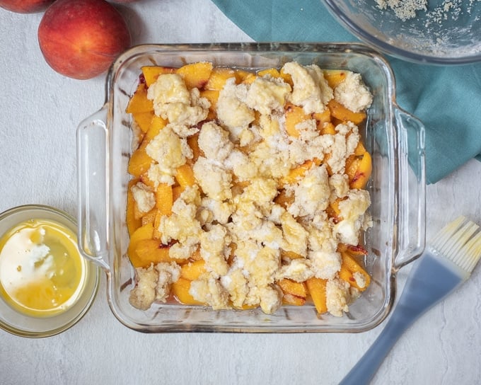 Biscuit Cobbler Topping spread over peaches in baking dish. 